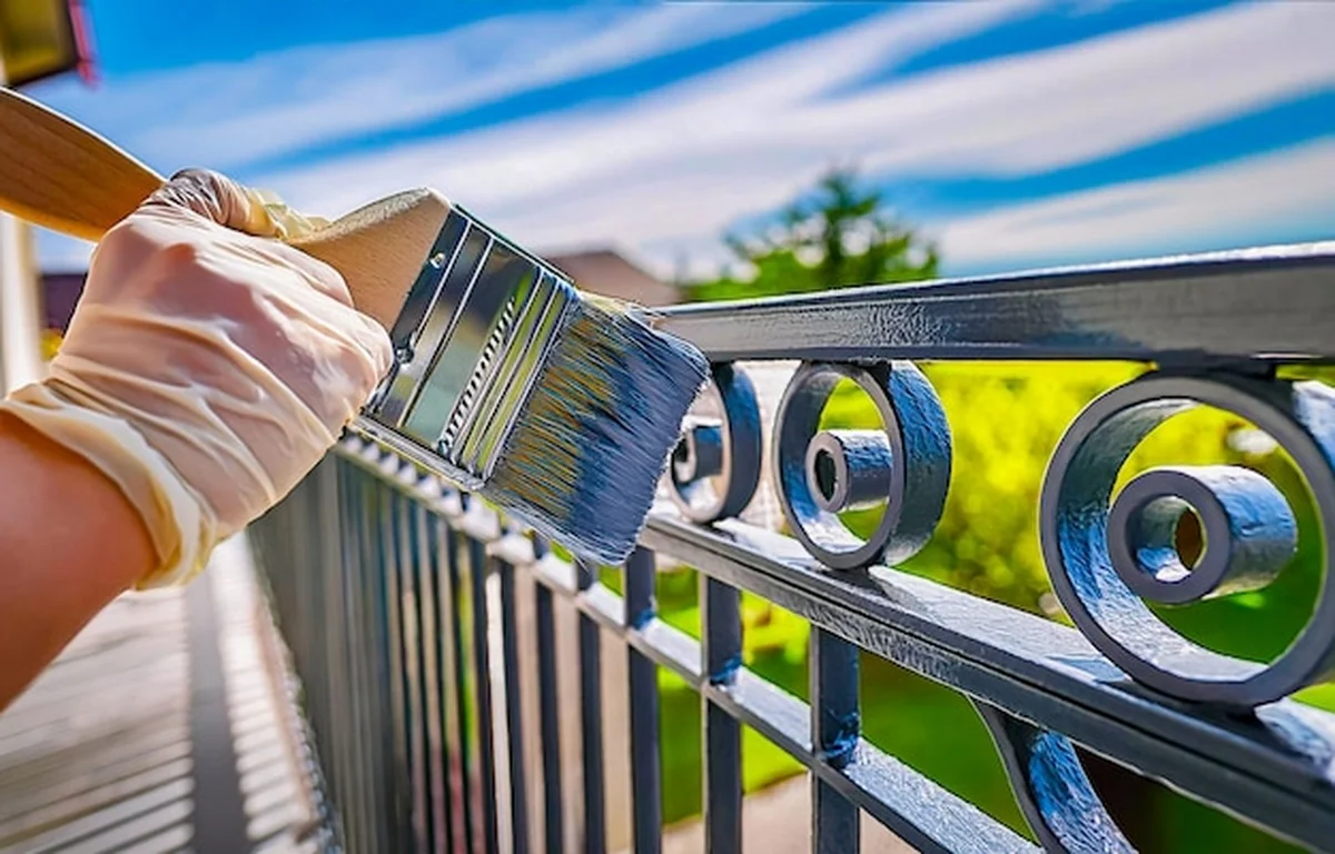 Malarz maluje szarą farbę na metalowej balustradzie balkonowej
