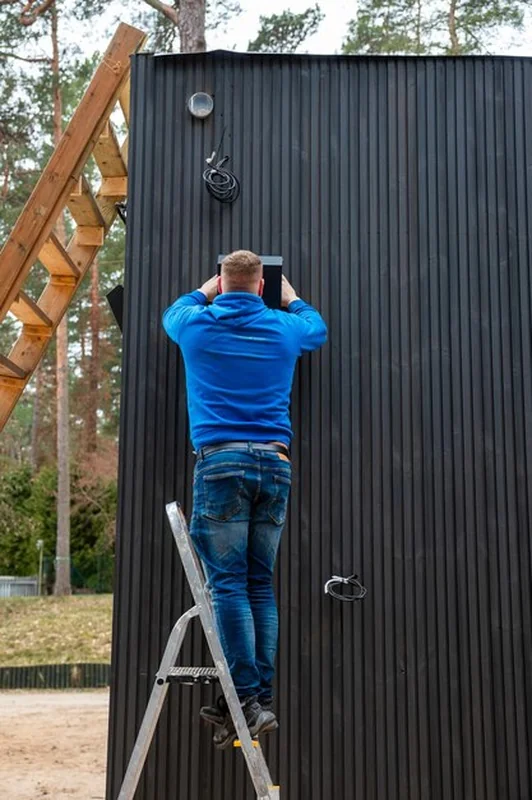 Mężczyzna na drabinie przy systemie wentylacyjnym z czarnymi panelami