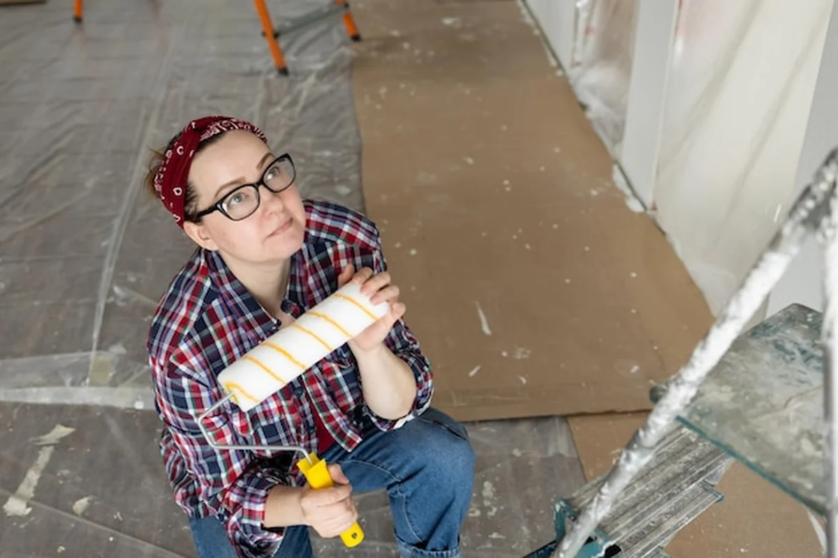 Piękna kobieta z rolką w rękach patrzy na ściany przed malowaniem