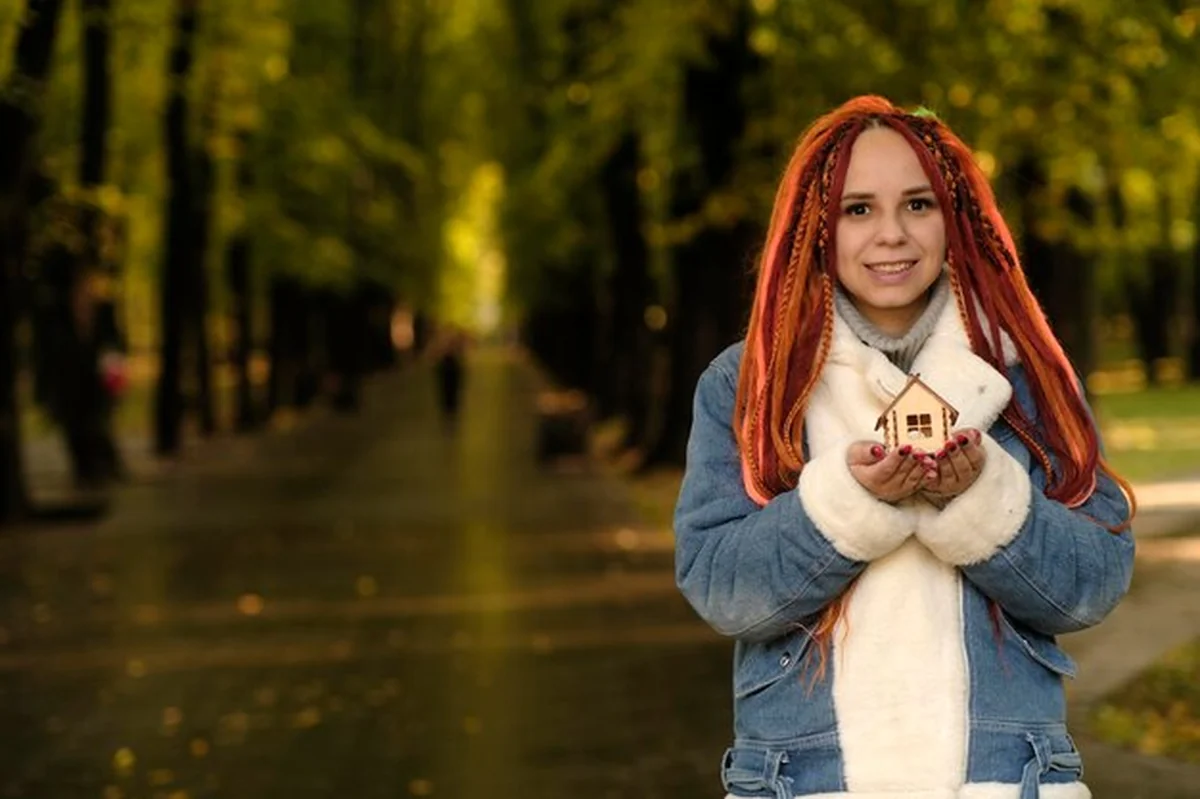 Uśmiechnięta kobieta trzymająca model domu w parku jesienią