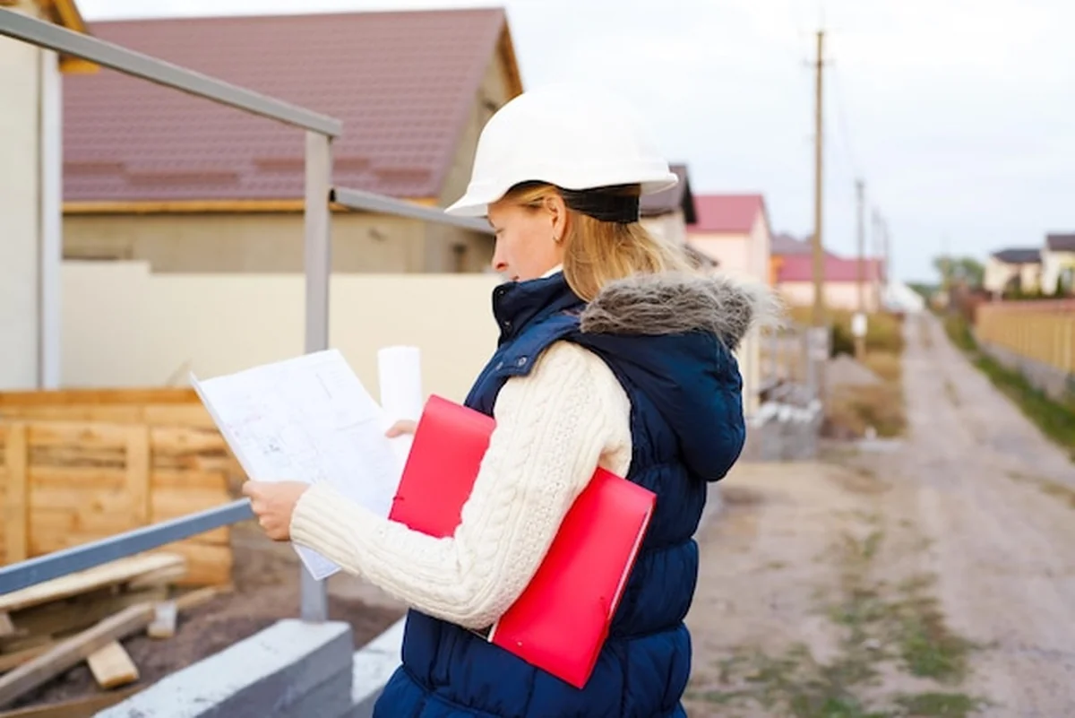 Kobieta w białym kasku z planem i schowkiem obok budynku