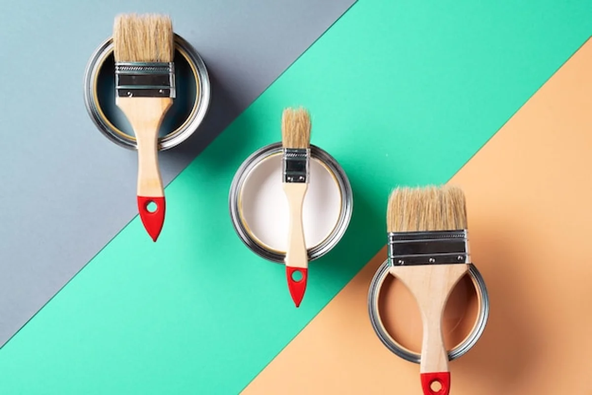 Metalowe puszki z farbą i pędzle na tle wielokolorowym, widok z góry, koncepcja modnego koloru zielonego