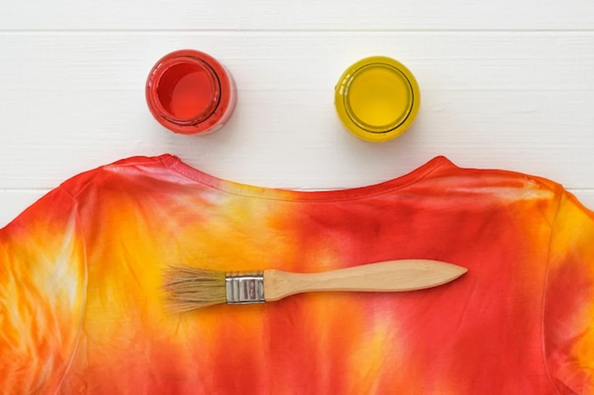 Pędzel, dwie puszki farby i jasny t-shirt z farbą na białym stole