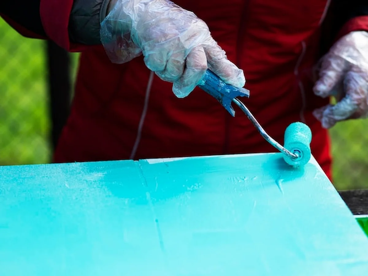 Ręka maluje arkusz sklejki rolką w kolorze turkusowym