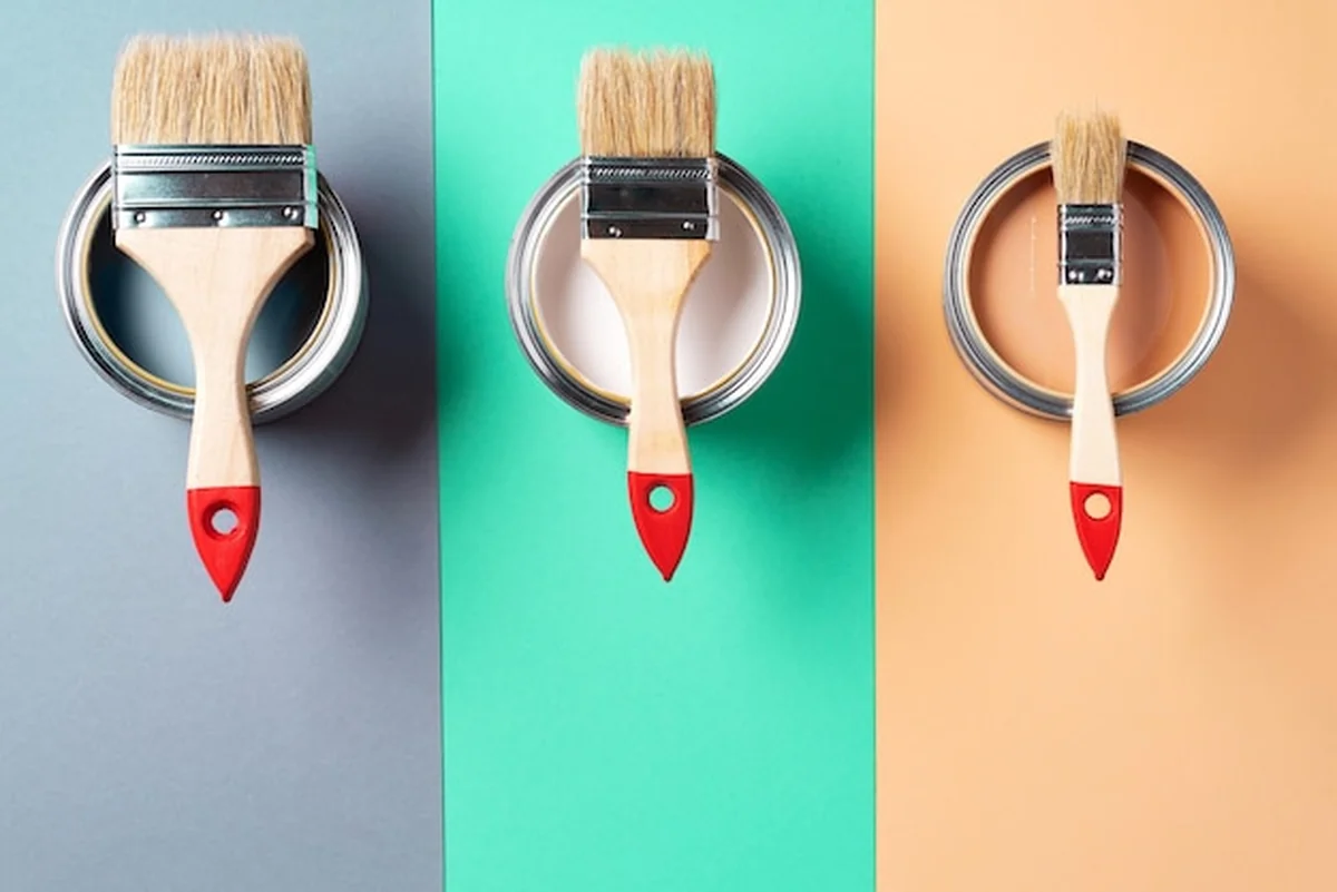 Metalowe puszki z farbą i pędzle na tle wielokolorowym, widok z góry