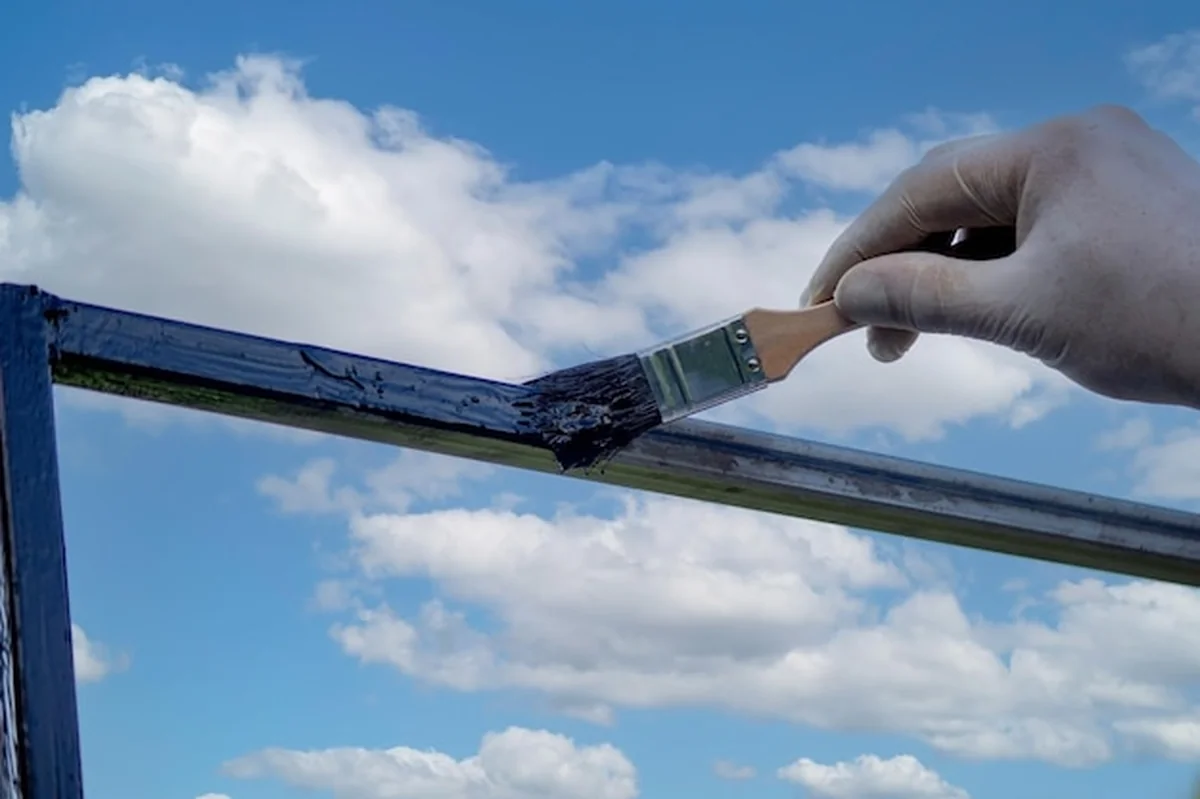 Mężczyzna maluje metalowy przedmiot czarną farbą pędzlem