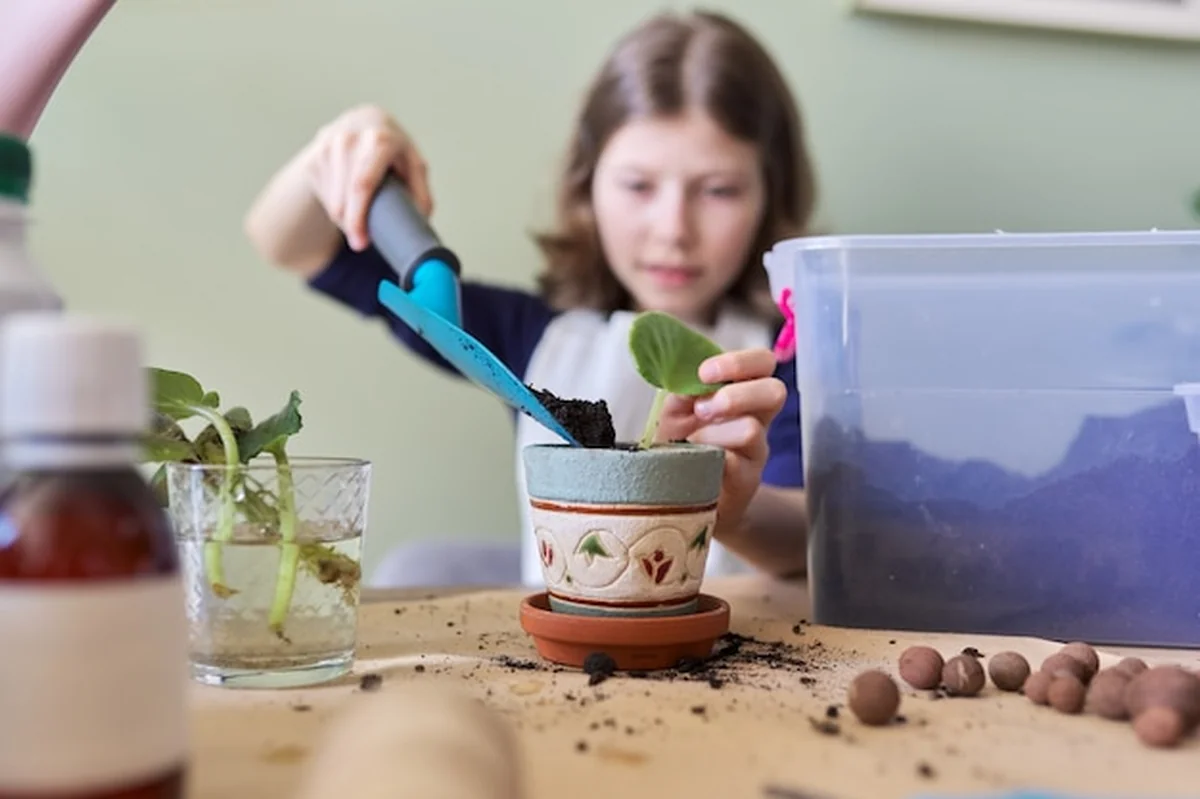 Dziewczynka sadzi liść rośliny w doniczce przy użyciu szpatułki i konewki